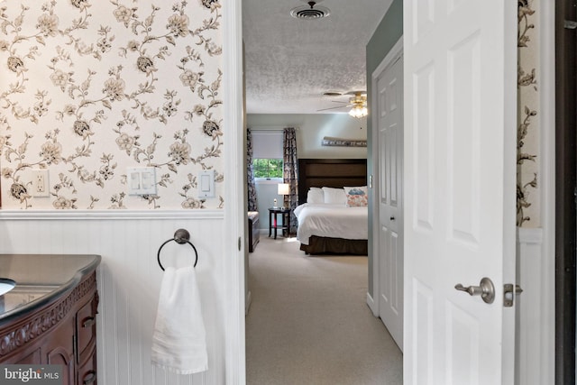 bathroom with a textured ceiling, a wainscoted wall, and ceiling fan