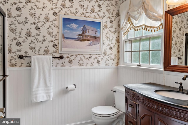 bathroom featuring wainscoting, toilet, wallpapered walls, and vanity