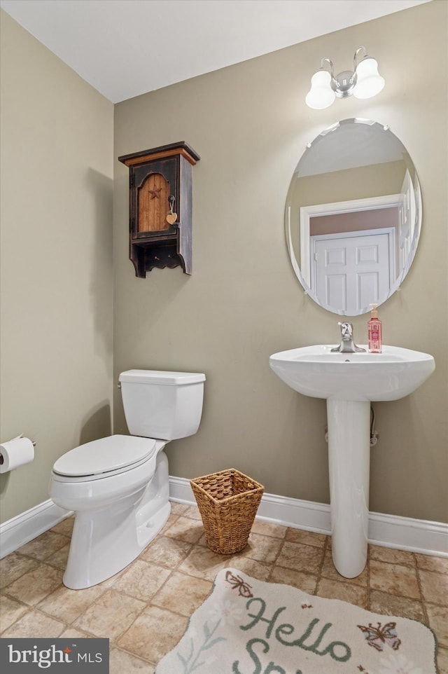 half bath featuring baseboards, toilet, and stone finish flooring