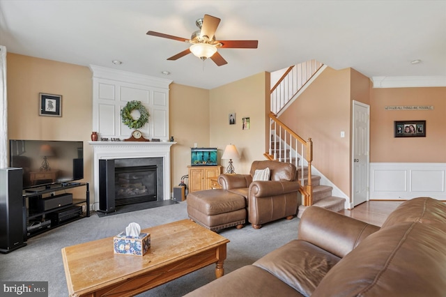 living room with a ceiling fan, carpet flooring, stairs, a fireplace, and ornamental molding