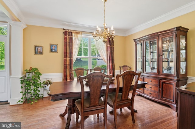 dining area with a chandelier, crown molding, light wood-style floors, a wainscoted wall, and ornate columns
