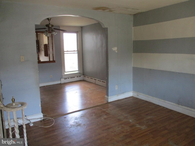empty room with arched walkways, ceiling fan, wood finished floors, and baseboards