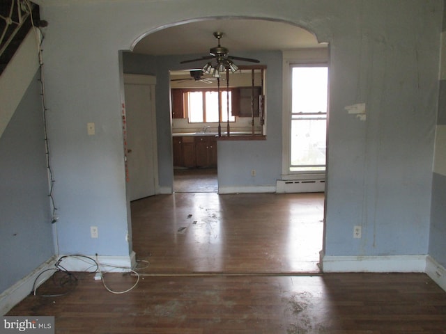 spare room with arched walkways, a ceiling fan, a baseboard heating unit, light wood-style flooring, and baseboards