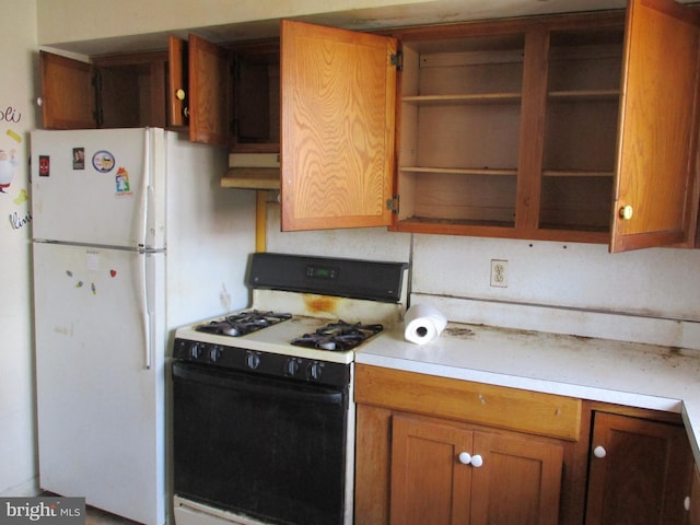kitchen with range with gas cooktop, open shelves, light countertops, brown cabinets, and freestanding refrigerator