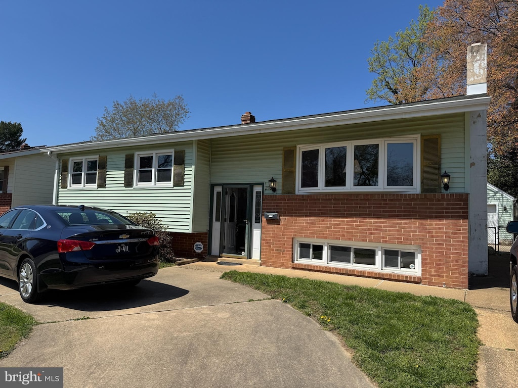 raised ranch with brick siding, driveway, and a chimney