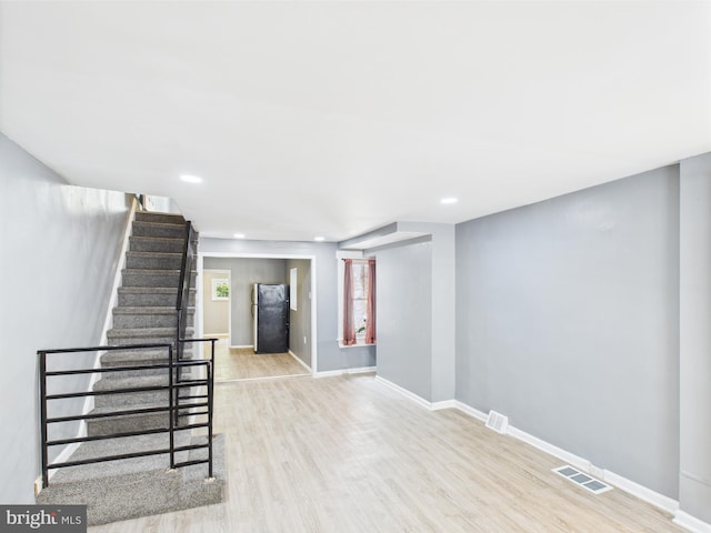 basement featuring stairs, wood finished floors, freestanding refrigerator, visible vents, and baseboards