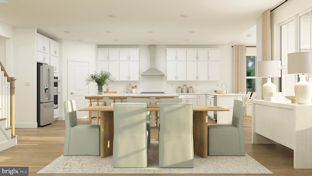 kitchen with light wood finished floors, white cabinetry, wall chimney exhaust hood, light countertops, and appliances with stainless steel finishes