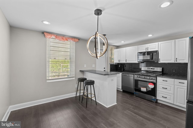 kitchen featuring appliances with stainless steel finishes, dark countertops, white cabinetry, a breakfast bar area, and baseboards