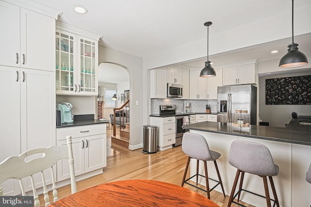 6226 Long Meadow Dr, Sykesville, MD 21784 - kitchen featuring stainless steel appliances, dark countertops, arched walkways, a kitchen breakfast bar, and light wood-style floors