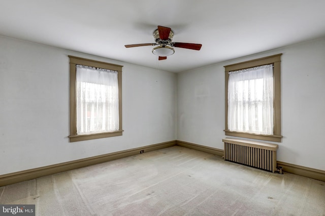 carpeted spare room featuring radiator heating unit, plenty of natural light, a ceiling fan, and baseboards