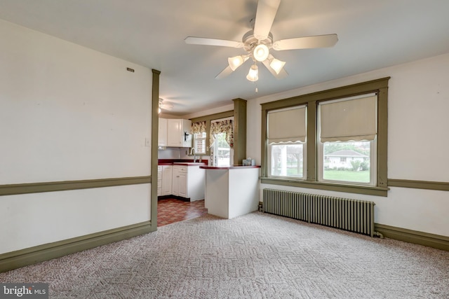 unfurnished living room featuring radiator heating unit, carpet flooring, a ceiling fan, a sink, and baseboards