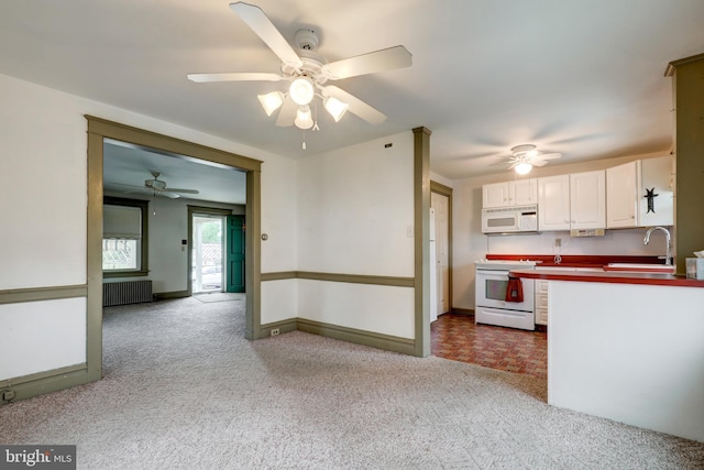 kitchen featuring white appliances, radiator, white cabinets, a sink, and a ceiling fan