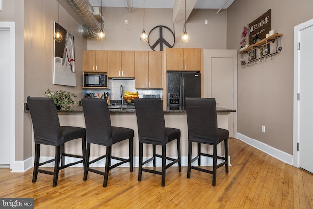 kitchen with a breakfast bar area, a peninsula, a towering ceiling, black appliances, and tasteful backsplash