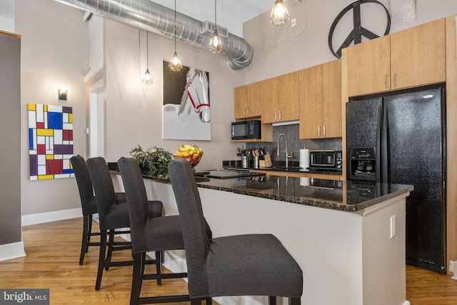 kitchen featuring a sink, tasteful backsplash, black appliances, a breakfast bar area, and a high ceiling