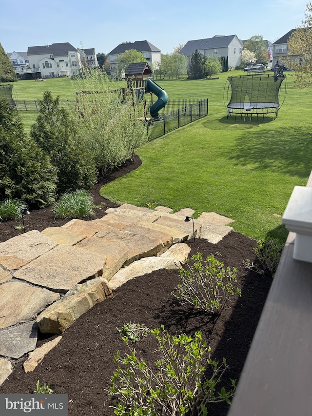 view of yard featuring a trampoline, a residential view, a playground, and fence