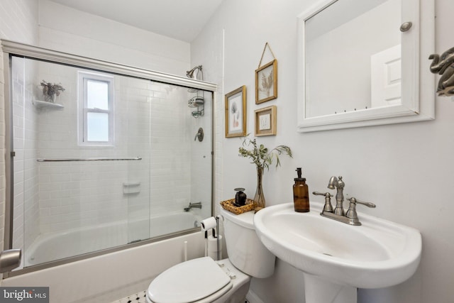 bathroom featuring toilet, a sink, and bath / shower combo with glass door