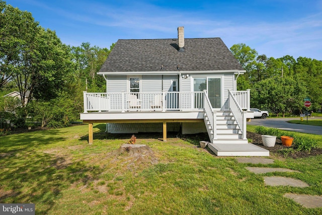 rear view of house with roof with shingles, a deck, a chimney, and a lawn
