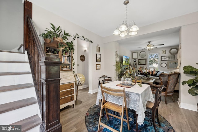 dining room with baseboards, stairway, ceiling fan with notable chandelier, and wood finished floors