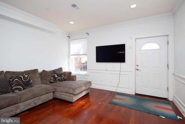 living area with crown molding, wood finished floors, visible vents, and a decorative wall