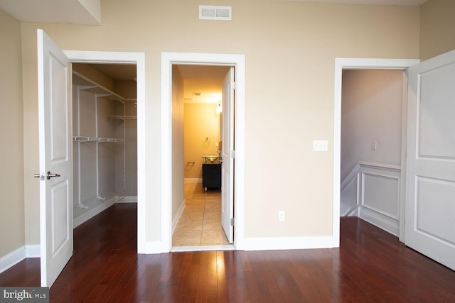 unfurnished bedroom featuring a closet, baseboards, visible vents, a walk in closet, and hardwood / wood-style floors