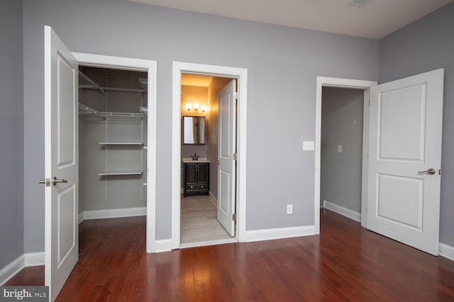 unfurnished bedroom with a spacious closet, a closet, baseboards, and wood finished floors