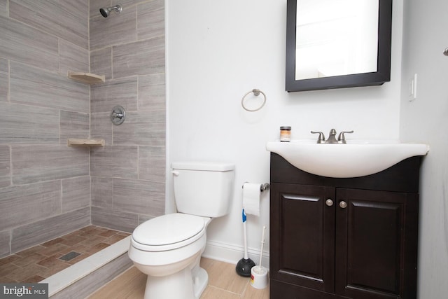 bathroom featuring vanity, toilet, baseboards, and tiled shower