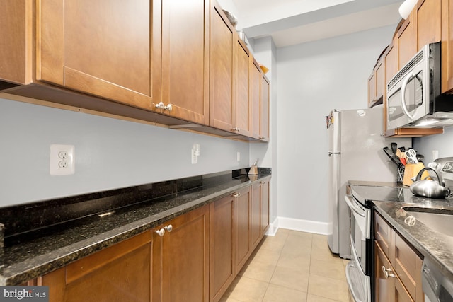 1613 Harvard St NW Unit 105, Washington, DC 20009 - kitchen featuring appliances with stainless steel finishes, light tile patterned floors, baseboards, dark stone counters, and brown cabinetry