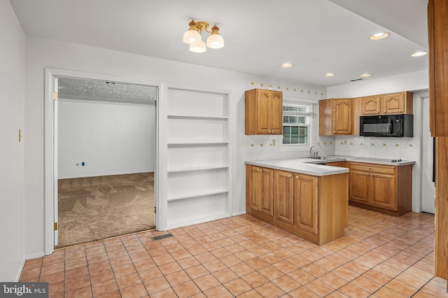 kitchen with black microwave, light countertops, a peninsula, a sink, and built in shelves