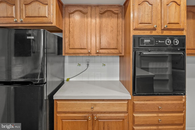 kitchen with black appliances, tasteful backsplash, brown cabinets, and light countertops