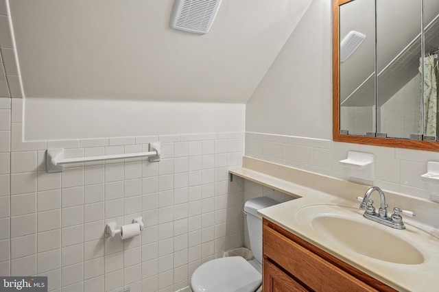 full bath featuring tile walls, toilet, vanity, lofted ceiling, and a wainscoted wall