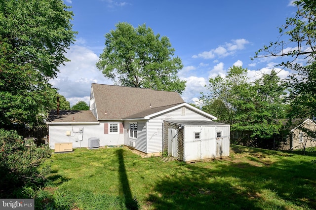 rear view of house with central AC unit, a storage unit, an outdoor structure, and a shingled roof