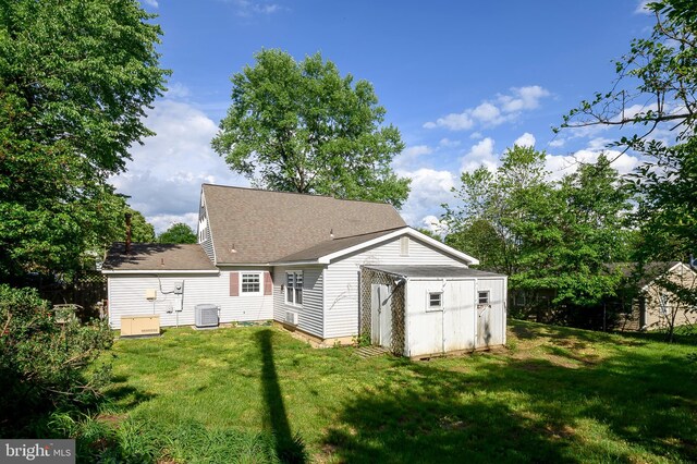 rear view of house with central AC unit, a storage unit, an outdoor structure, and a shingled roof
