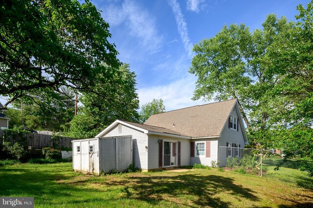 back of house with a storage unit, an outbuilding, and a shingled roof