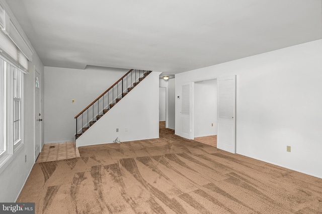 unfurnished living room featuring carpet floors, stairway, and baseboards