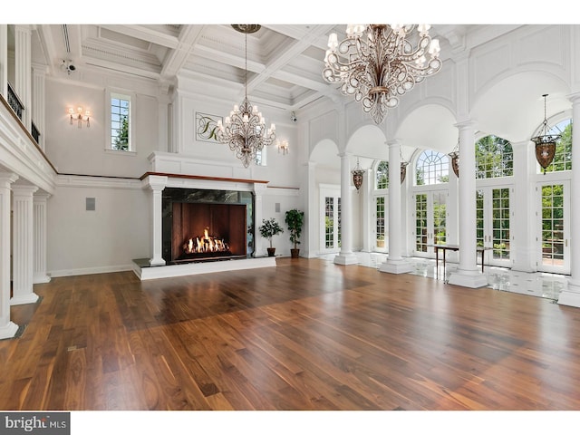 unfurnished living room featuring wood finished floors, coffered ceiling, beam ceiling, a fireplace, and a towering ceiling