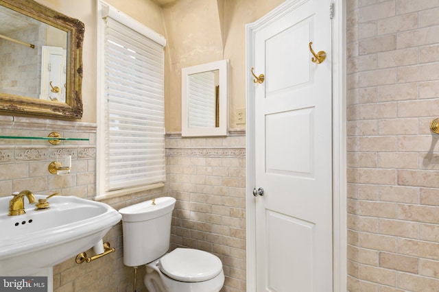bathroom with a sink, wainscoting, tile walls, and toilet