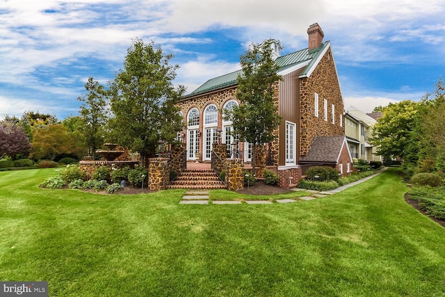 view of front facade featuring stone siding, a chimney, a front yard, and a standing seam roof