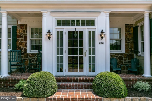 doorway to property featuring stone siding, french doors, and covered porch