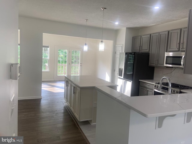 kitchen featuring stainless steel appliances, a kitchen island, gray cabinets, tasteful backsplash, and wood finished floors