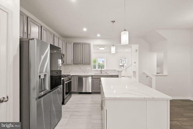 kitchen featuring appliances with stainless steel finishes, gray cabinetry, a center island, light stone countertops, and a sink