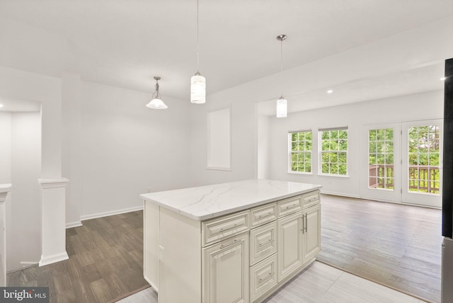 kitchen featuring light wood finished floors, light stone countertops, hanging light fixtures, a center island, and baseboards