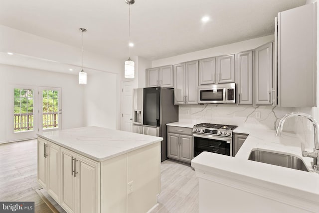 kitchen featuring stainless steel appliances, a sink, gray cabinetry, a center island, and backsplash