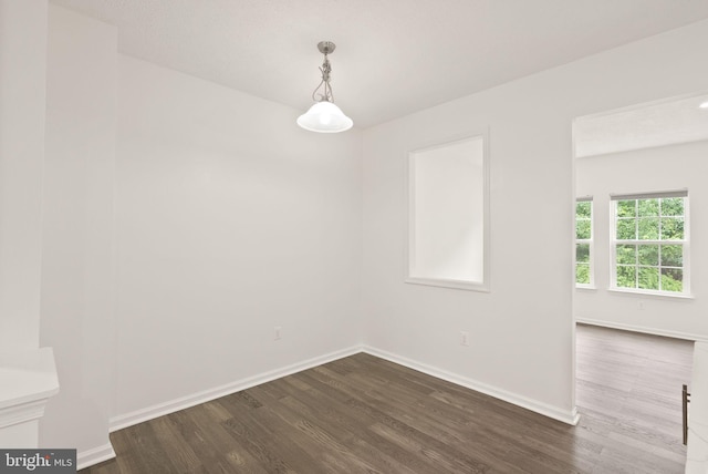 spare room featuring dark wood-style flooring and baseboards