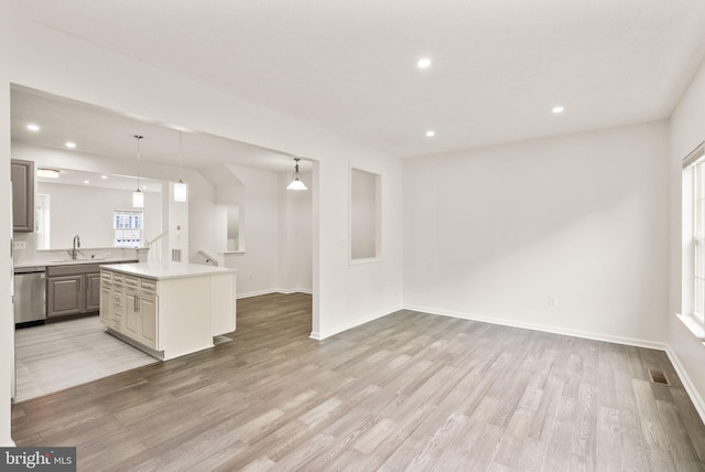 unfurnished living room with light wood finished floors, recessed lighting, a sink, and baseboards