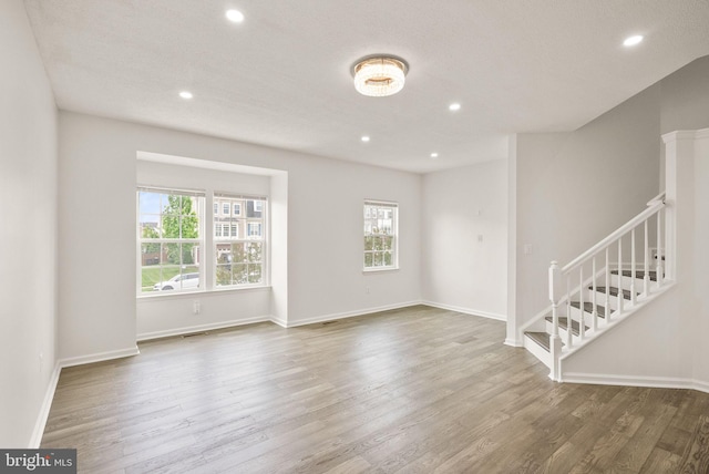 unfurnished living room with stairs, wood finished floors, recessed lighting, and baseboards