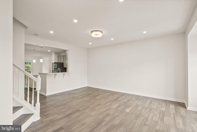 unfurnished living room featuring recessed lighting, wood finished floors, stairway, and baseboards