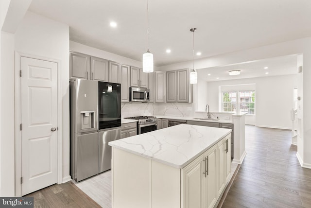 kitchen featuring stainless steel appliances, a sink, a kitchen island, recessed lighting, and gray cabinetry