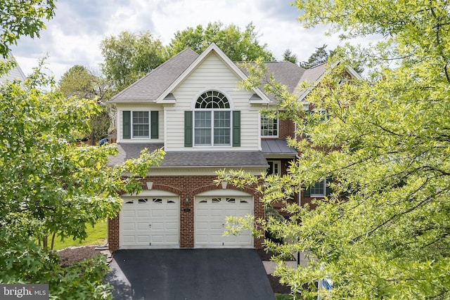 exterior space with an attached garage, a shingled roof, brick siding, and driveway