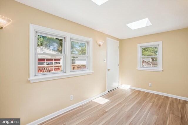 unfurnished room with a skylight, healthy amount of natural light, wood finished floors, and baseboards