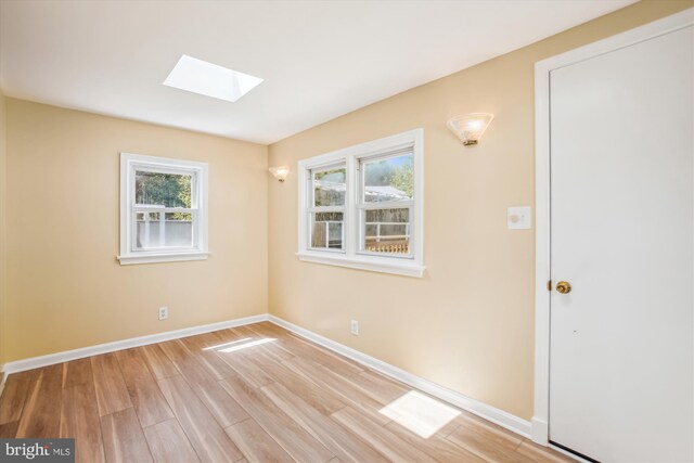 unfurnished room with a skylight, light wood finished floors, and baseboards